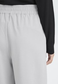 Pantalon de survêtement gris clair avec une taille élastique, une texture lisse et une coupe décontractée, associé à un haut à manches longues noir.