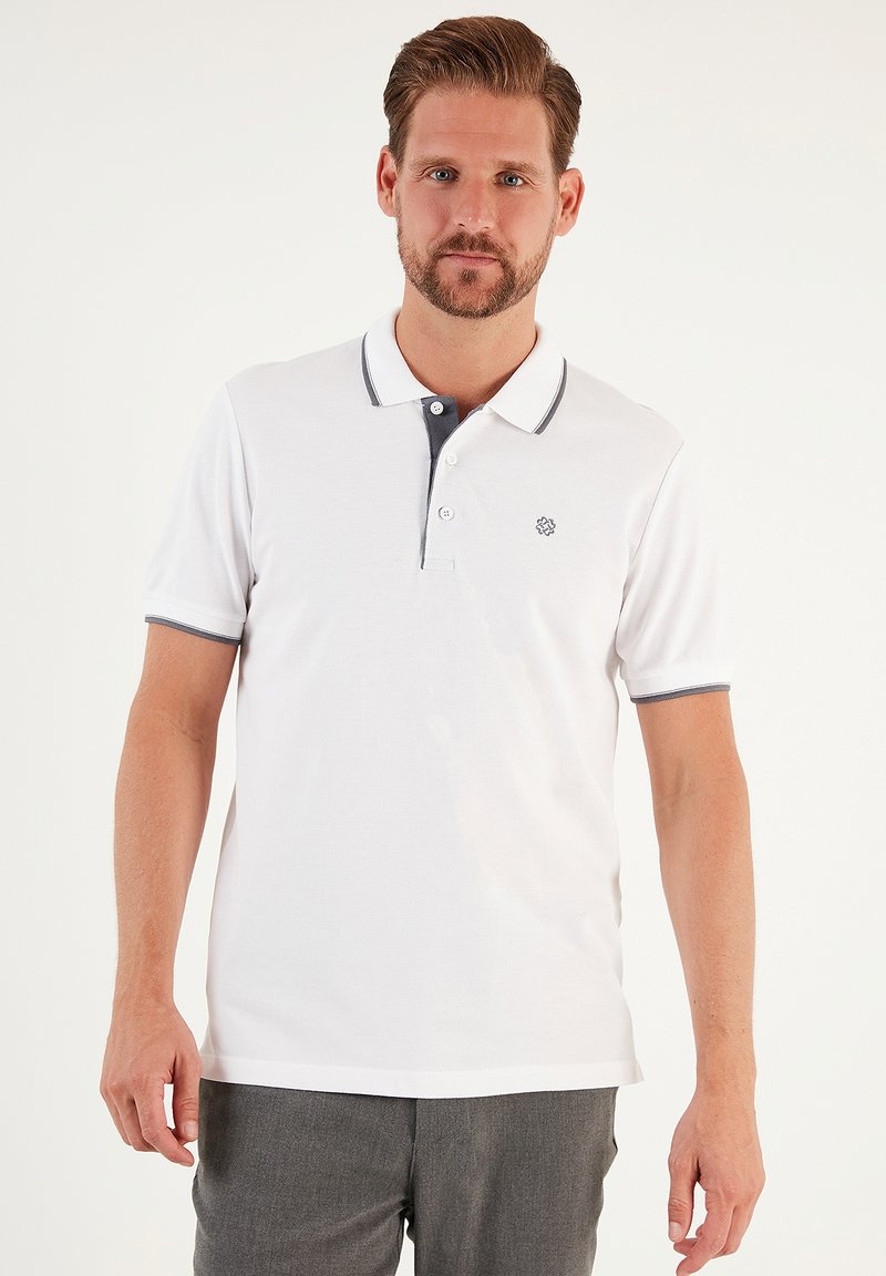 Polo bianco con dettagli grigi; maniche corte, patta con due bottoni e un piccolo emblema sul lato sinistro del petto. Texture liscia.
