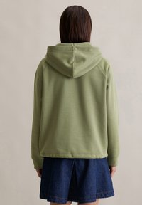 Olijfgroen hoodie met een ontspannen pasvorm, voorzien van een kangoeroezak en ribgebreide manchetten, gecombineerd met een denimrok.