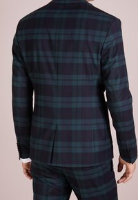 Navy en groen geruite blazer met een getailleerde pasvorm, voorzien van een enkele split, inkepingen en met knoopmanchetten. Gelaagd stof.