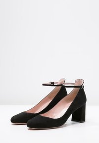 Schwarze Wildleder-High Heels mit quadratischem Absatz, spitzer Zehenform und Knöchelriemen. Das Innenfutter hat eine weiche rosa Farbe.
