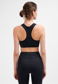 Svart sport-bh med racerback-design, sömlös finish och mjuk textur, i kombination med högmidjade svarta leggings som har en dragkedjeficka.