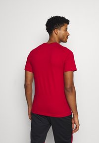 Rød kortærmet t-shirt lavet af glat stof, med en rund hals og et simpelt design. Udsigten er fra bagsiden, som viser den tætsiddende form.