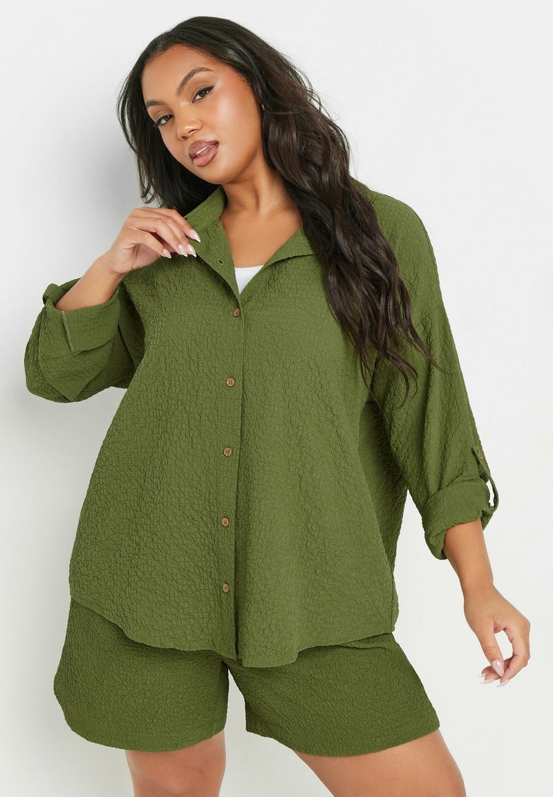 Camicia corta a maniche con colletto e bottoni, di colore verde oliva e struttura texturizzata, abbinata a pantaloni corti coordinati, caratterizzati da una vestibilità comoda e un motivo sottile.