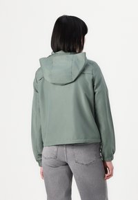 Light green, hooded jacket with a cropped design, elastic cuffs, and a smooth texture. Back view highlights stitching and streamlined shape.