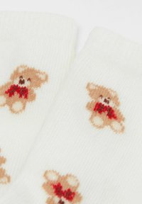 Calzini bianchi con lavorazione a maglia testurata, con un motivo ripetuto di piccoli orsetti marroni con fiocchi rossi.