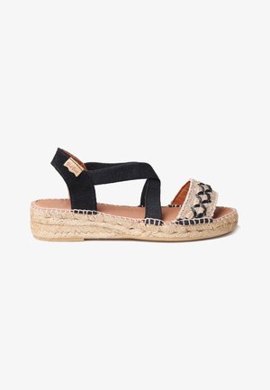 Black woven fabric cross-strap sandal with a natural jute braided sole and decorative stitching on the toe, featuring a tan leather tag.