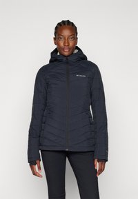Pufferjakke i marineblått, med hette, glidelås lukking og chevron-søm. Stoffet ser lett ut med elastiske mansjetter.