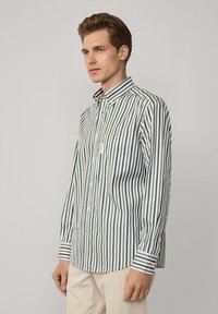 Camisa abotonada con un patrón de rayas verticales en verde y blanco, mangas largas, cuello en punta y un bolsillo en el pecho.
