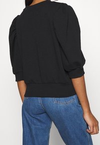 Black pullover with puff sleeves, ribbed hem, and a soft texture. Worn with blue denim jeans, showcasing a casual silhouette.