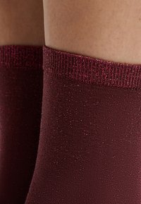 Calzini bordeaux in un morbido tessuto testurizzato con accenti lucenti. Il bordo a costine è elastico, offrendo una vestibilità sicura.