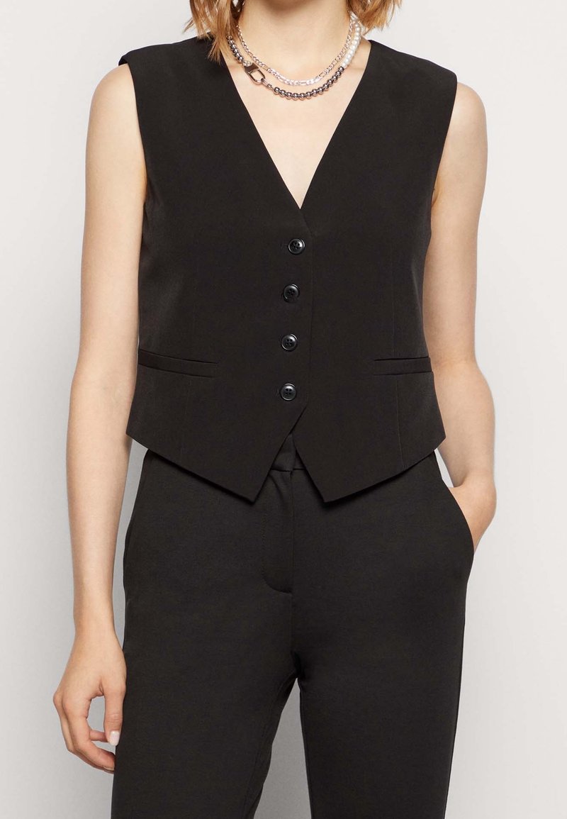 Gilet noir sans manches avec encolure en V profonde, fermeture à cinq boutons et deux poches avant ; design élégant et ajusté avec une texture de tissu lisse.