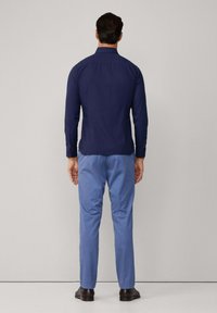 Marineblauw overhemd met lange mouwen en knoopmanchetten, gecombineerd met lichtblauwe broek en zwarte schoenen. Glad stof, slim fit, geen zichtbare patronen.