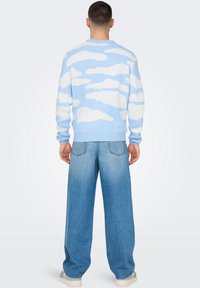Lichtblauwe gebreide trui met een wit wolkenpatroon, ronde hals en geribbelde manchetten, gedragen met losse lichtblauwe jeans.