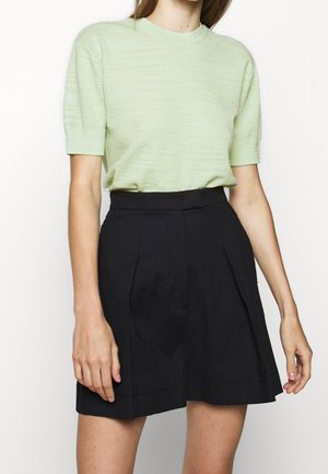 Helles grünes Kurzarm-Strickoberteil, kombiniert mit hochgeschnittenen schwarzen Falten-Shorts. Weiche Textur, schlichtes Design und klassischer Farbkombination.