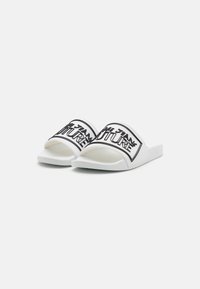 White slide sandals feature a wide band with black lettering that reads "FUTURE." The outsole is flat and textured for grip.