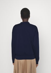 Navy blue sweatshirt with a ribbed waistband and cuffs, featuring a crew neck and drop shoulders, paired with a pleated beige skirt.