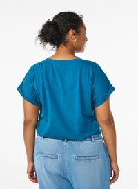Teal short-sleeve top with rolled sleeves, featuring a loose fit. Background is plain white, showcasing the garment's color and shape.