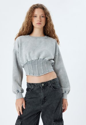 Felpa grigia corta con orlo a coste e maniche a palloncino, abbinata a pantaloni cargo in denim nero a vita alta. Texture liscia in tutto il capo.