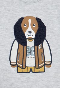 Un beagle de dessin animé portant une veste de lycée marron avec un col en fausse fourrure, un t-shirt blanc et un short jaune sur un fond gris.