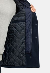 Marinejacke mit gesteppter Innenseite, verfügt über ein glattes Außmaterial, einen Reißverschluss und seitliche Taschen; strukturierte Innenauskleidung sichtbar.
