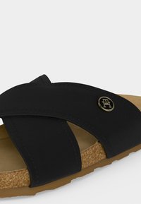 Μαύρο σανδάλι με χιαστί λουράκια, φελλό πάτο, ταμπά σόλα και μικρό στρογγυλό χρυσό λογότυπο στην εξωτερική πλευρά.