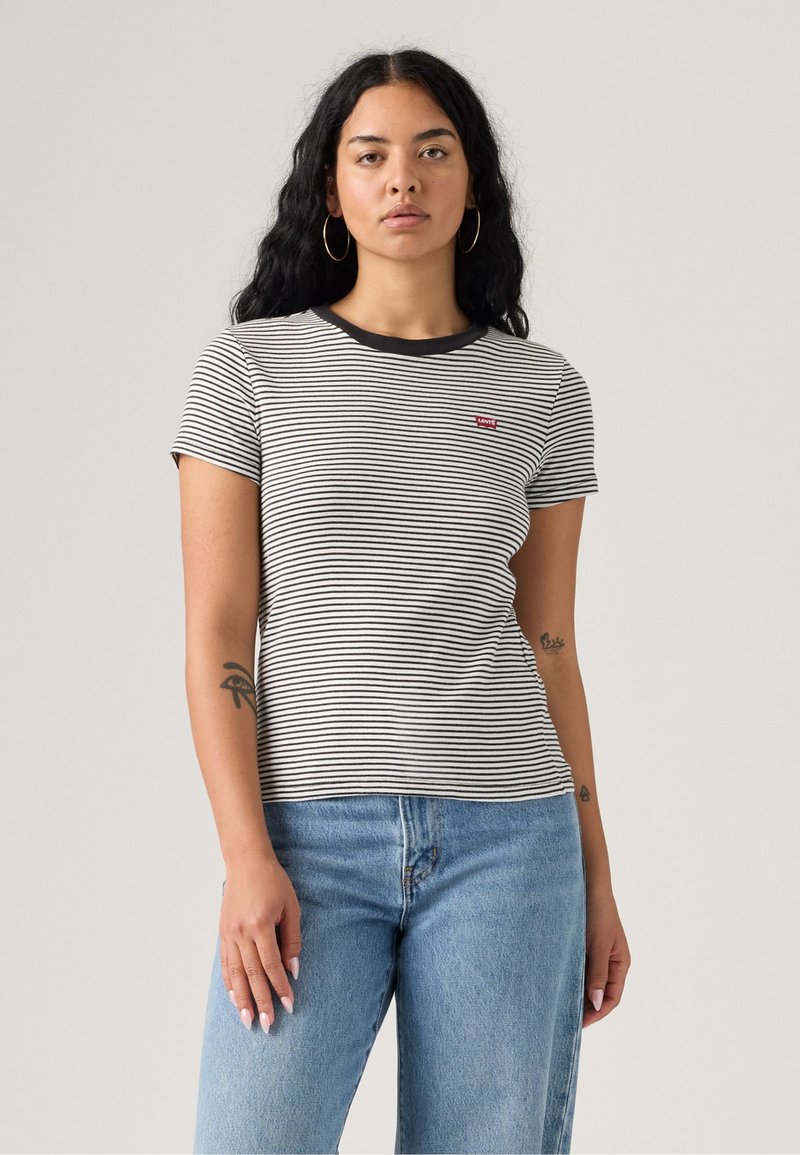 T-shirt à rayures à manches courtes noir et blanc, avec un col rond et un petit patch de logo rouge. Associé à un jean bleu clair.