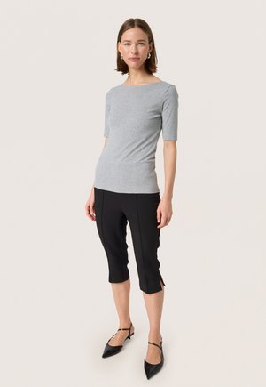 Top grigio aderente con maniche corte abbinato a pantaloni neri a tre quarti con spacchi laterali. Modella con scarpe slingback nere.