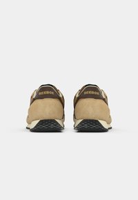 Biege nubuk tenisice s crnim detaljima, mekani ovratnik i teksturirana crna gumena potplata. Na stražnjem dijelu se nalazi zlatni "Reebok" logo.