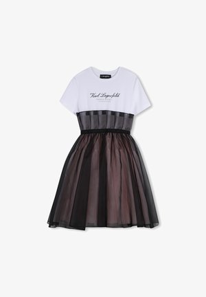 Bijela majica s crnim tekstom iznad višeslojne suknje od tila u različitim nijansama sive i crne, s crnim elastičnim pojasom.