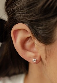 Orecchino a pendente in argento con design floreale, caratterizzato da numerosi piccoli gemelli trasparenti. Indossato in un orecchio forato, vista ravvicinata.