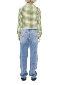 Veste cropped en pied-de-poule vert et blanc avec col, manches longues, associée à un jean bleu clair à coupe ample, doté de poches arrière.