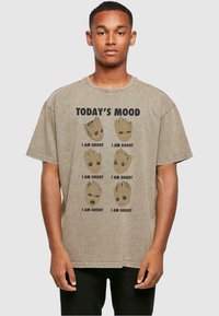 Pruun ülisuur t-särk, millel on mitu joonistust Grooti nägudest ja tekst "TÄNANE MEELDOLK" ning "MA OLE JAA GROOT." Puuvillane materjal.