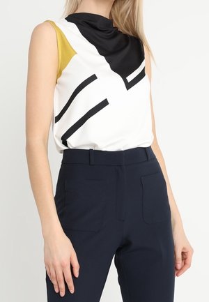 Biały top bez rękawów z czarnymi, żółtymi i geometrycznymi wzorami; miękka tkanina; w duecie z granatowymi spodniami z wysokim stanem i przednimi kieszeniami.
