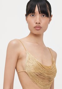 Mesh bralette in gold, featuring a draped fringe design. Thin straps and a smooth underlayer create a layered texture and elegant shape.