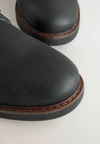 Zwarte leren boots met ronde neuzen, decoratieve stiksels langs de zool en een gestructureerde, matte afwerking op het bovenmateriaal.