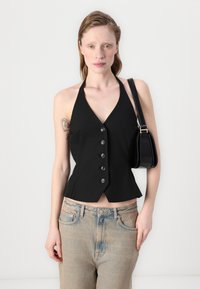 Svart halterneck crop topp med en tettsittende silhuett, med fem knapper foran og en peplumhem, kombinert med lyse vaskede jeans.