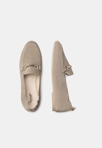Beige Wildleder-Loafer mit flacher Sohle, ausgestattet mit einer dekorativen goldenen Kettenakzent und einem weichen Innenfutter. Flacher Absatz und runde Zehenform.