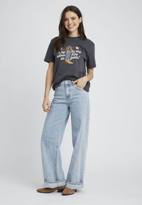 T-shirt en coton gris foncé avec un imprimé graphique, associé à un jean large bleu clair et des bottines beiges. Pas de motifs ou de quincaillerie distincts.