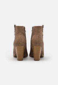 Brune ankelstøvler med glat tekstur, lynlås bagpå og en stablet, ribbet hæl. Har minimalistisk design og neutral farve.