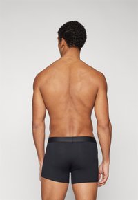 Schwarze trunkartige Unterwäsche mit glattem Bund, tailliertem Design und einfacher, nahtloser Textur, von hinten betrachtet.