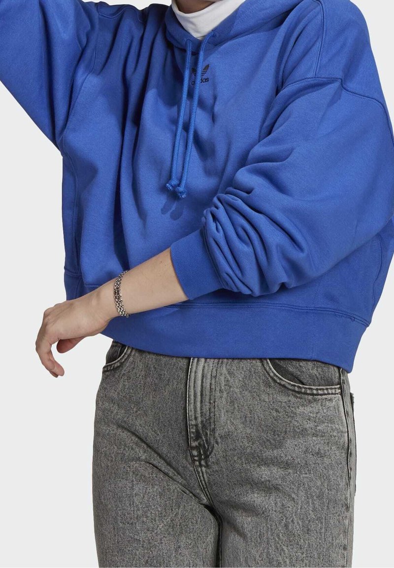 Haut cropped bleu avec capuche à cordon, poignets côtelés et un petit logo sur la poitrine, associé à un jean en denim gris taille haute.