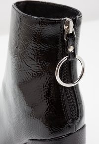 Schwarze Lackstiefelette mit strukturiertem Finish, runden silbernen Beschlägen und einem seitlichen Reißverschluss für einfaches An- und Ausziehen.