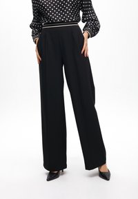 Black wide-leg trousers made of a smooth fabric, featuring a high waist and side pockets. Paired with a polka dot blouse.