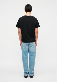 Μαύρο κοντομάνικο T-shirt από βαμβάκι, συνδυασμένο με ανοιχτό μπλε τζιν παντελόνι σε άνετη εφαρμογή με τσέπες στο πίσω μέρος, από την πίσω όψη.