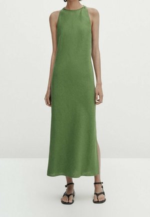 Zielona, bezrękawnikowa sukienka maxi z wysokim dekoltem, gładką fakturą, rozcięciem po boku i minimalistycznym designem, zestawiona z czarnymi płaskimi sandałami.