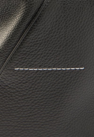 Czarna skórzana torba z teksturowaną powierzchnią, wyraźnymi kątami oraz białym przeszyciem wzdłuż szwu jako kontrastującym detalem.