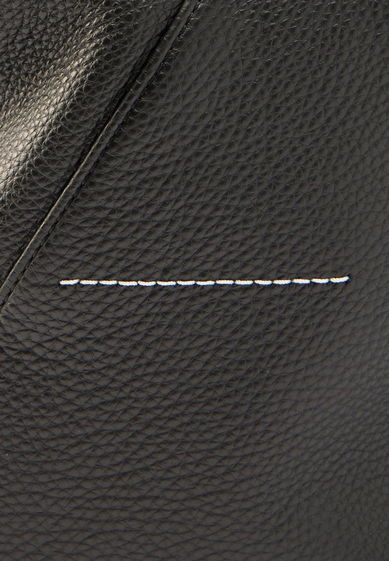 Black leather bag featuring textured exterior, sharp angles, and white stitching detail along a seam for contrast.