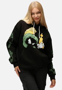 Felpa nera in cotone, con una grande grafica di un personaggio dei cartoni animati in verde e giallo sul davanti, e stampe sulle maniche.