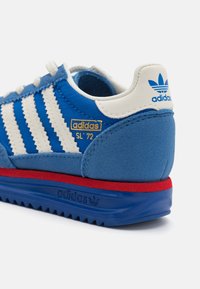 Blå mocka och textil sneakers med vita ränder och röda accenter, med guld-logotypen "adidas SL '72" på hälen och strukturerad sula.